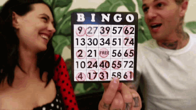 a man and woman are playing bingo and the man is holding up a bingo card