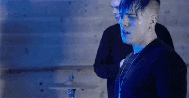 two men are playing drums in a dark room in a blue light .