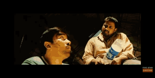 two men are sitting next to each other in a dark room and talking to each other .