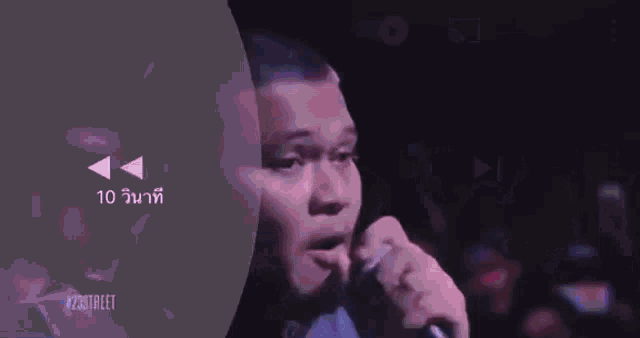 a man is singing into a microphone in a dark room with a purple background .