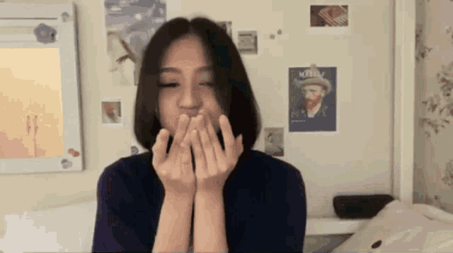a woman covering her mouth with her hands in front of a wall with a poster of van gogh on it