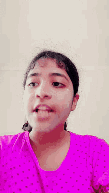 a girl wearing a pink shirt with white polka dots is making a face