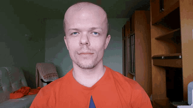 a bald man with a beard wears an orange t-shirt