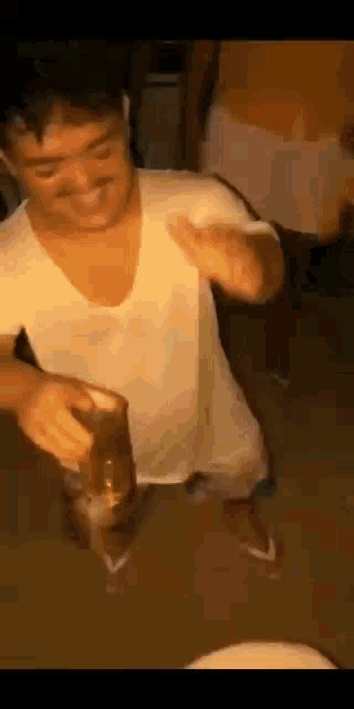 a man in a white shirt is holding a glass of beer while dancing in a room .