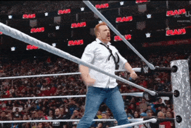 a man in a white shirt and tie is in a wrestling ring with the word raw on the wall