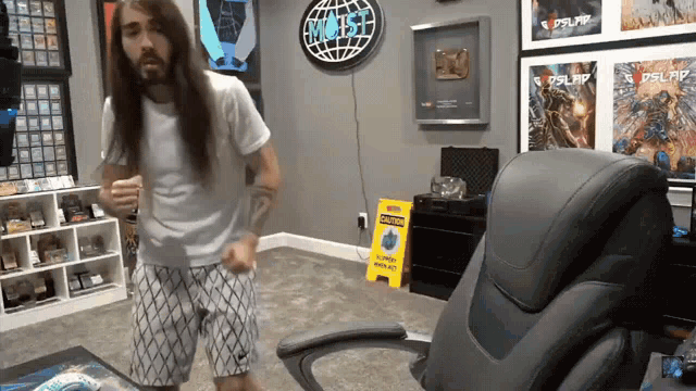 a man with long hair is dancing in a room with a yellow sign that says " caution wet floor "