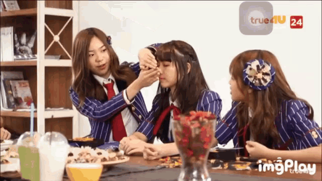a group of girls are sitting at a table with a vase of flowers in front of them and a screen that says true4u 24