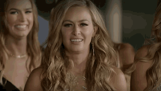 a woman with long blonde hair is smiling in front of a group of women