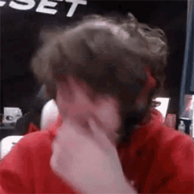 a man in a red shirt is touching his face with his hand .