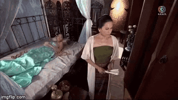 a woman in a green top is standing next to a bed with a green blanket .