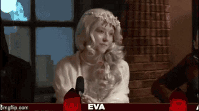 a woman in a white wig is sitting in front of a microphone with the name eva on the bottom of the screen