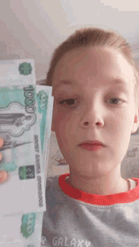 a young boy is holding a 1000 ruble bill