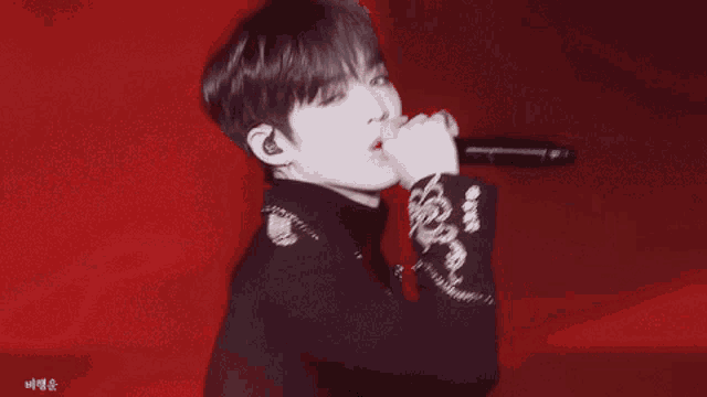 a close up of a person singing into a microphone with a red background