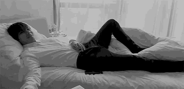 a man in a white shirt and black pants is laying on a bed with his legs crossed .