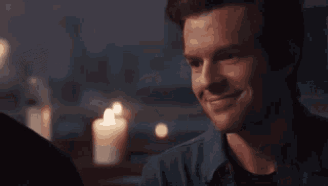 two men are sitting at a table in front of candles .