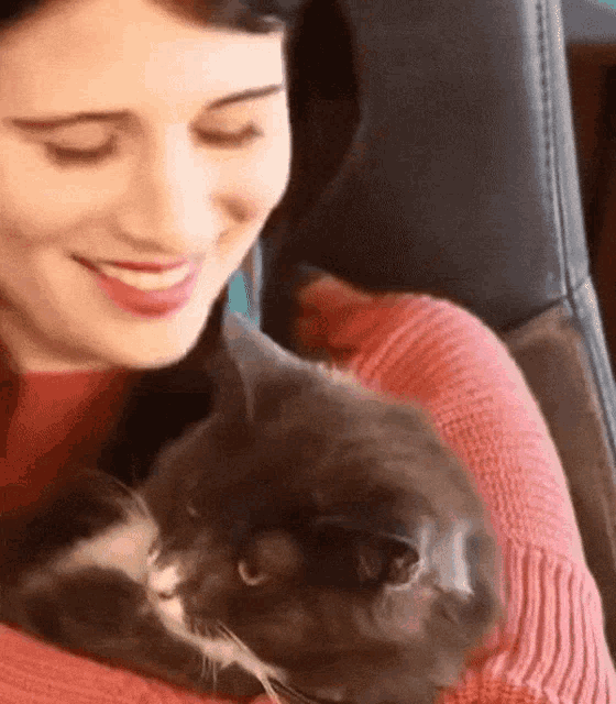 a woman in a red sweater is holding a cat in her arms