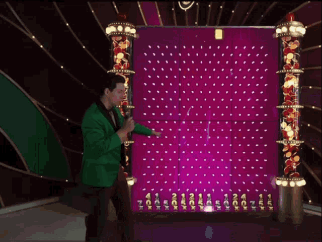 a man in a green jacket holds a microphone in front of a pink wall