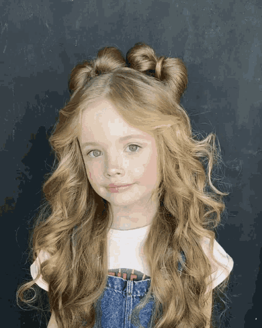 a little girl with long blonde hair is wearing overalls