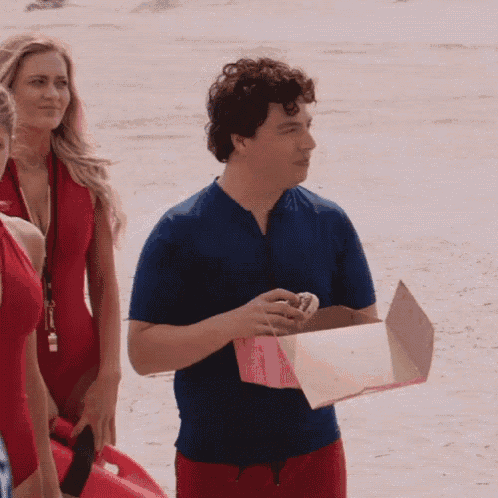 a man in a blue shirt is holding a pink box on a beach