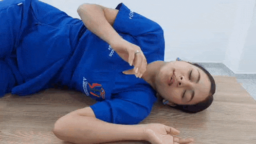 a woman in a blue scrub top is laying on a wooden floor .