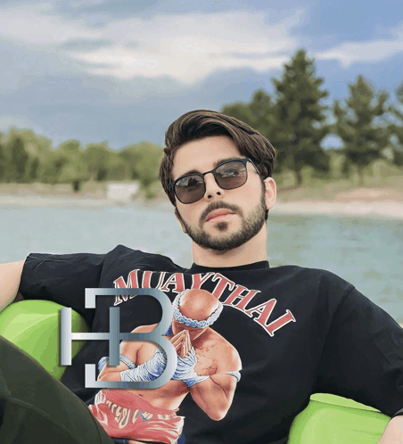 a man wearing sunglasses and a muaythai shirt sits on a green raft