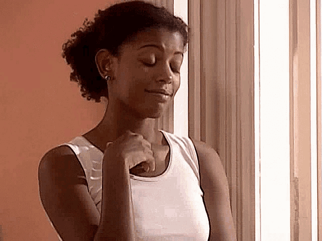 a woman is standing in front of a window with her eyes closed and her hands folded .