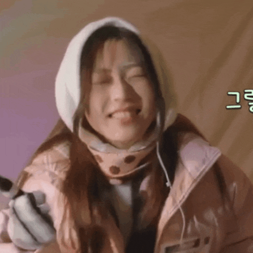 a woman wearing a pink jacket and a white hood is smiling with her eyes closed