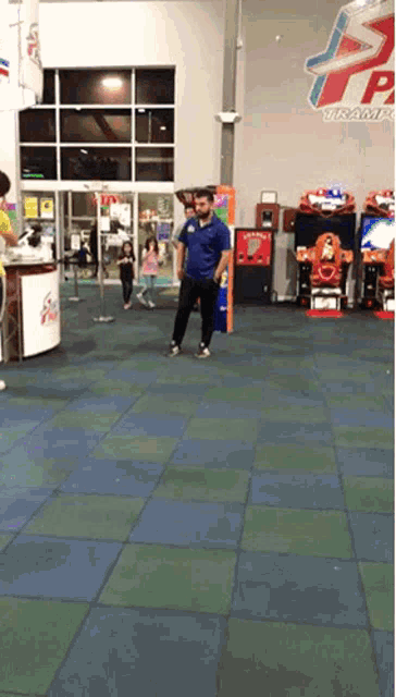 a man in a blue shirt stands in an arcade with a sign that says ' tp ' on it