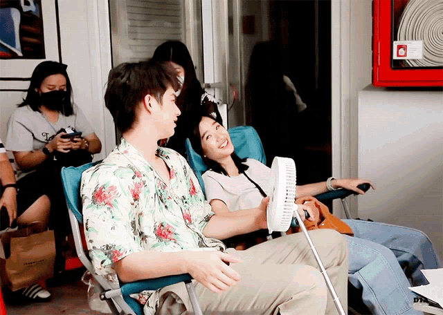 a man and a woman are sitting in chairs in front of a fire extinguisher