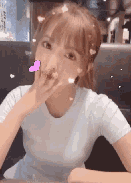 a woman is sitting at a table with her hand on her face and a heart on her face .