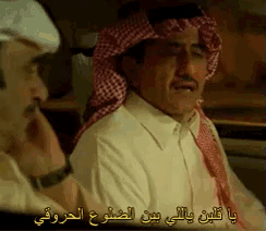 a man wearing a head scarf and a white shirt is speaking in arabic