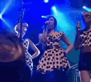 a woman in a polka dot dress sings into a microphone on a stage