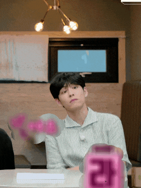 a man sitting at a table with a pink cube that says ' 라 ' on it
