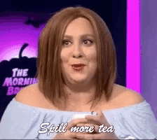 a woman in a wig is holding a cup of tea and saying spill more tea .
