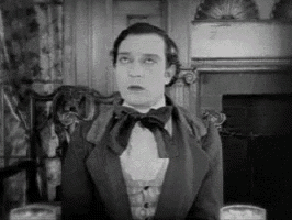a man in a suit and bow tie is sitting in front of a fireplace in a black and white photo .