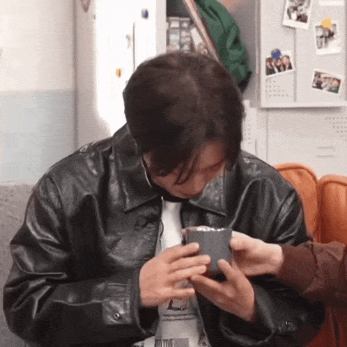 a man wearing a black leather jacket is holding a cup of coffee