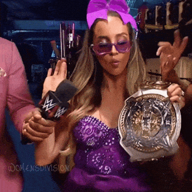 a woman in a purple dress is holding a wrestling trophy and wearing sunglasses