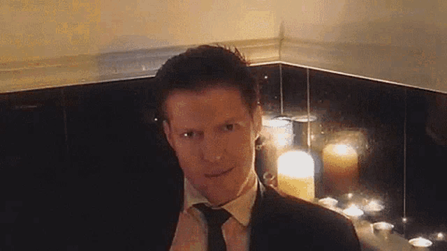 a man in a suit and tie is standing in front of candles in a bathroom