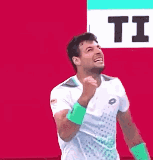 a man wearing a white shirt and green wristbands is holding his fist up in the air .