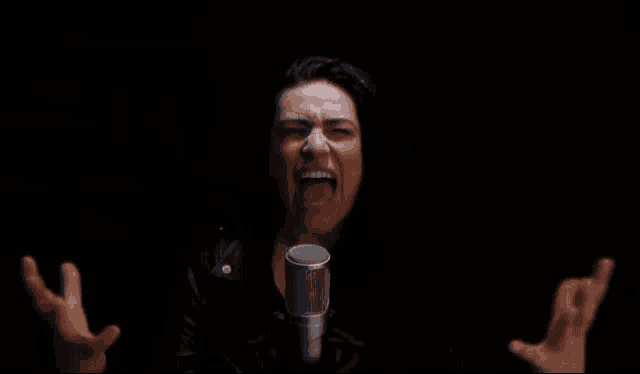 a woman is singing into a microphone with her mouth open and her hands in the air .