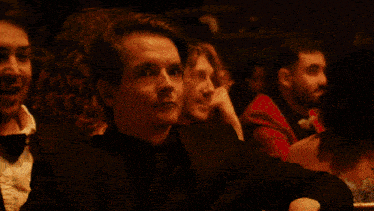 a man in a tuxedo and bow tie is surrounded by other people