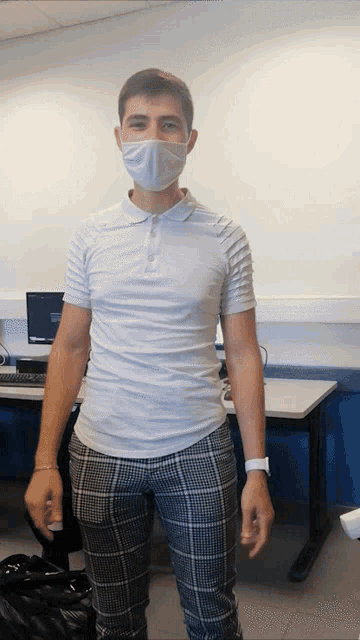 a man wearing a mask and plaid pants stands in front of a desk