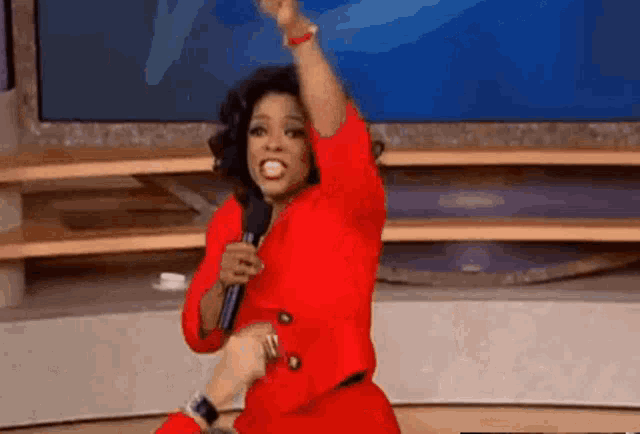 oprah winfrey is wearing a red dress and holding a microphone while dancing on a stage .