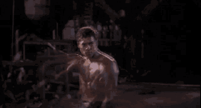 a man without a shirt is standing in a dark room with his arms outstretched