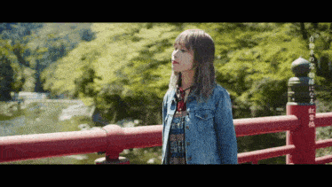 a woman in a denim jacket is standing on a bridge