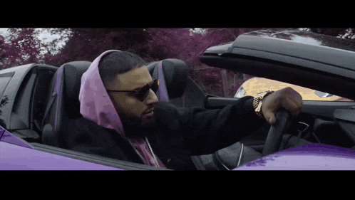 a man wearing a pink hoodie is driving a purple sports car