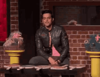 a man in a leather jacket is sitting at a table with plates of food .