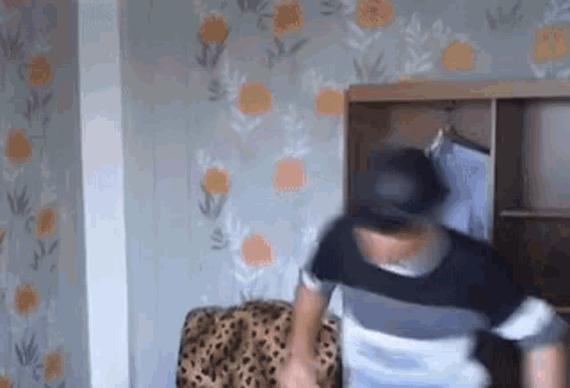 a man in a hat is standing in a room with a leopard print chair .