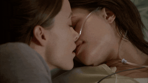two women kissing in a hospital bed with an oxygen tube in her neck