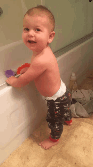 a baby in a diaper stands in front of a bath tub